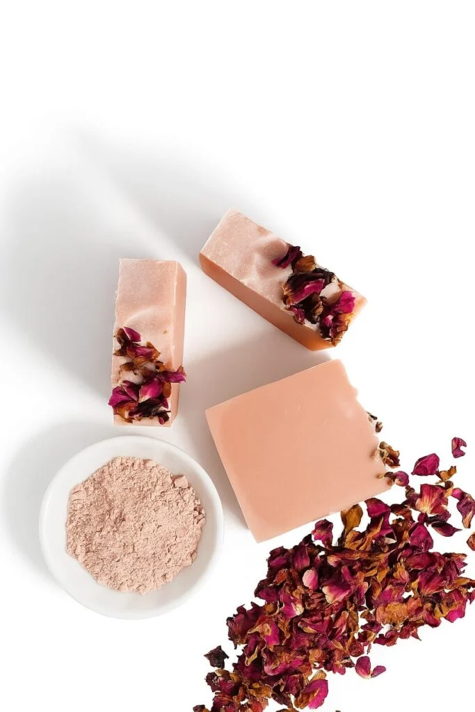 A hand holding a pink rose clay soap bar topped with dried rose petals