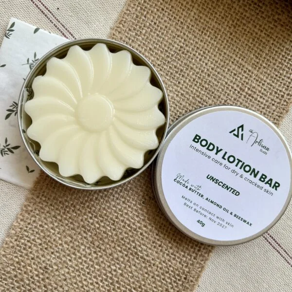 Unscented body lotion bar with a flower design in an open tin, next to its labelled lid