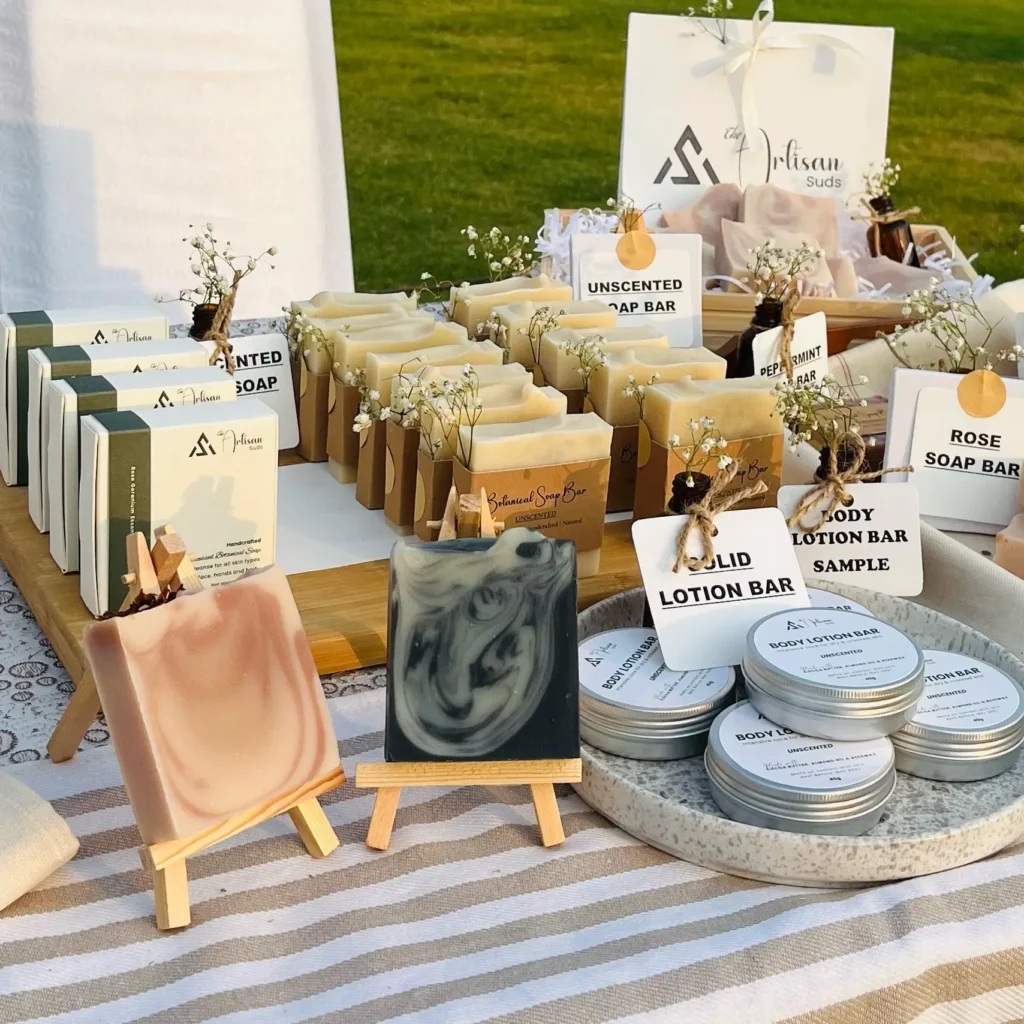 The Artisan Suds handmade soaps and body lotion bar tins displayed on a table